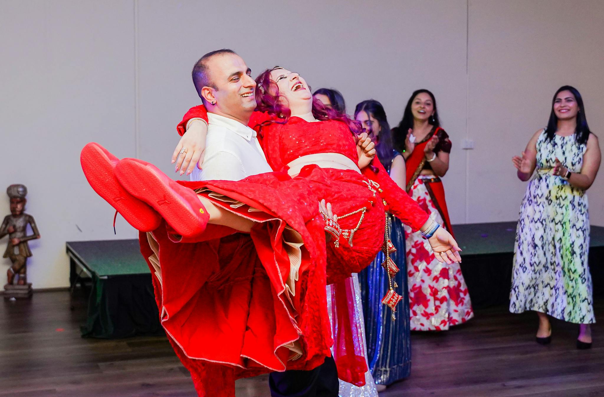 A man joyfully carries a woman in a vibrant dress during a fun, lively dance party.
