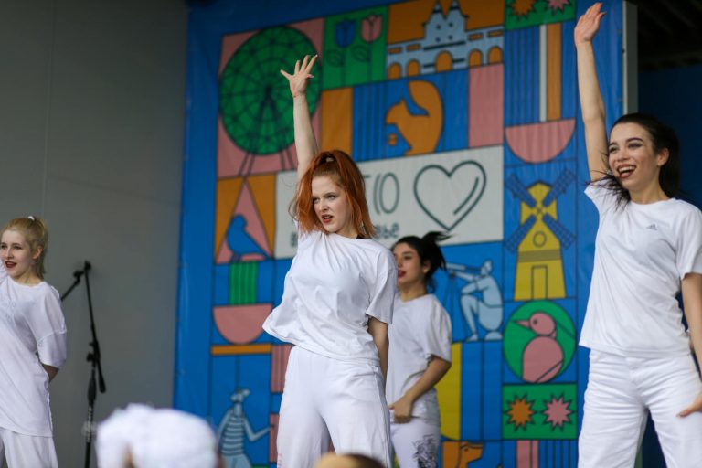 Dynamic group dance performance with diverse women in white outfits on a colorful mural stage.