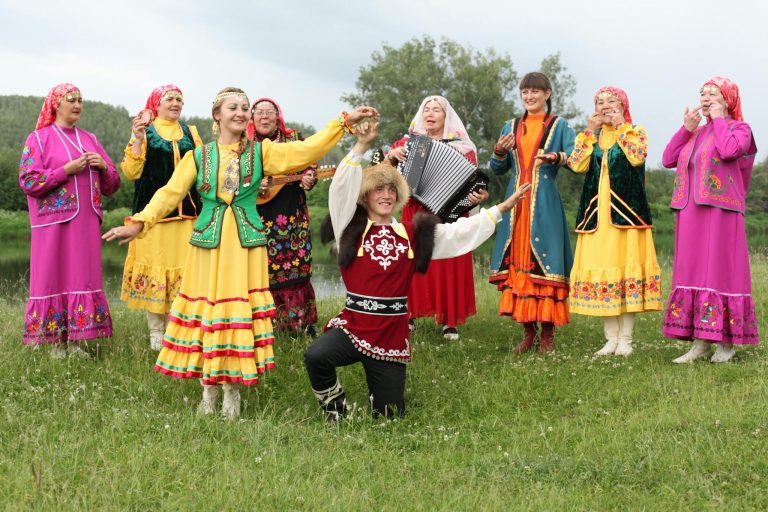 Group of people in traditional costumes enjoying folk dance and music in a field.