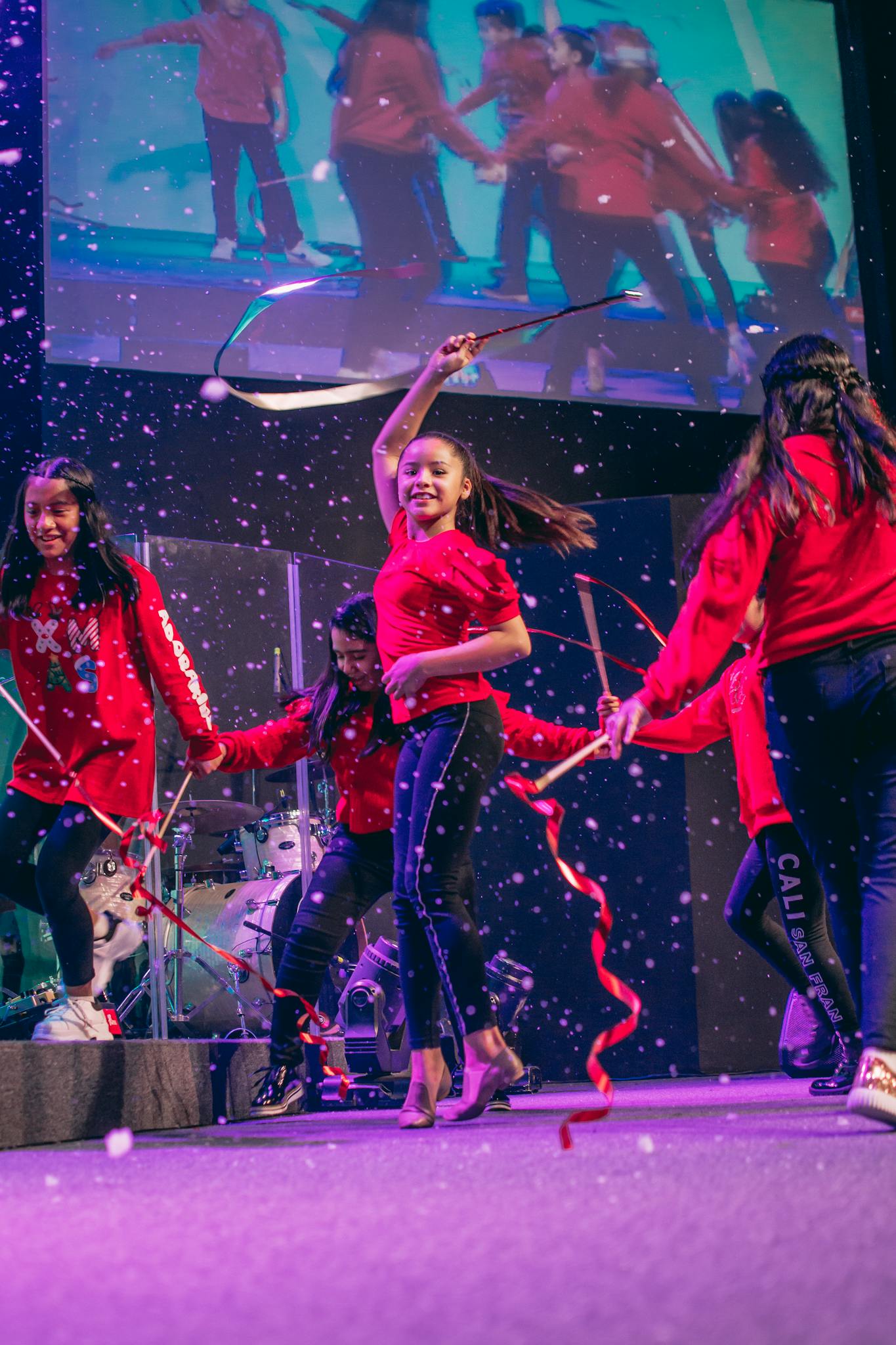 Group of young dancers performing energetically on stage with vibrant ribbons, creating a lively atmosphere.