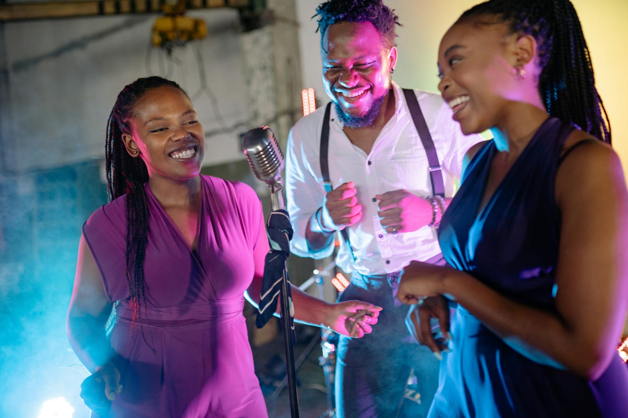 Three smiling adults enjoy singing and dancing in a lively, colorful setting indoors.